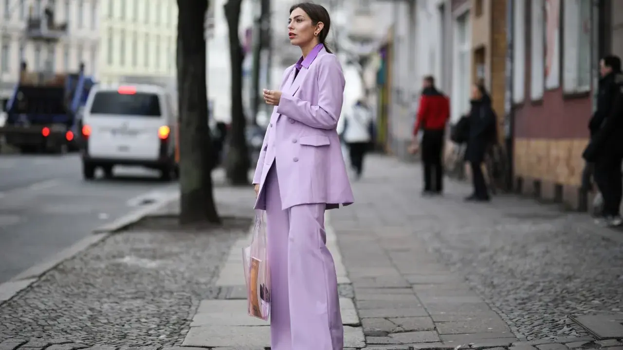 Elegancka kobieta w garniturze w kolorze liliowym, stojąca na brukowanym chodniku.