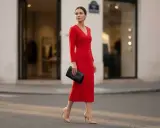 Elegancka kobieta w czerwonej sukience i cielistych szpilkach, niosąca czarną kopertówkę. Idealne buty do czerwonej sukienki na wieczorne wyjście.