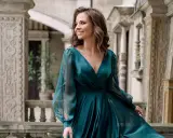 Kobieta w eleganckiej, turkusowej sukni, idealnej na coctail attire, uśmiecha się na tle zabytkowej architektury.