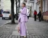 Elegancka kobieta w garniturze w kolorze liliowym, stojąca na brukowanym chodniku.