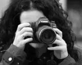 Czarno-białe zdjęcie kobiety z kręconymi włosami, która trzyma aparat Canon. To jej pierwsze szkolenie z fotografii.