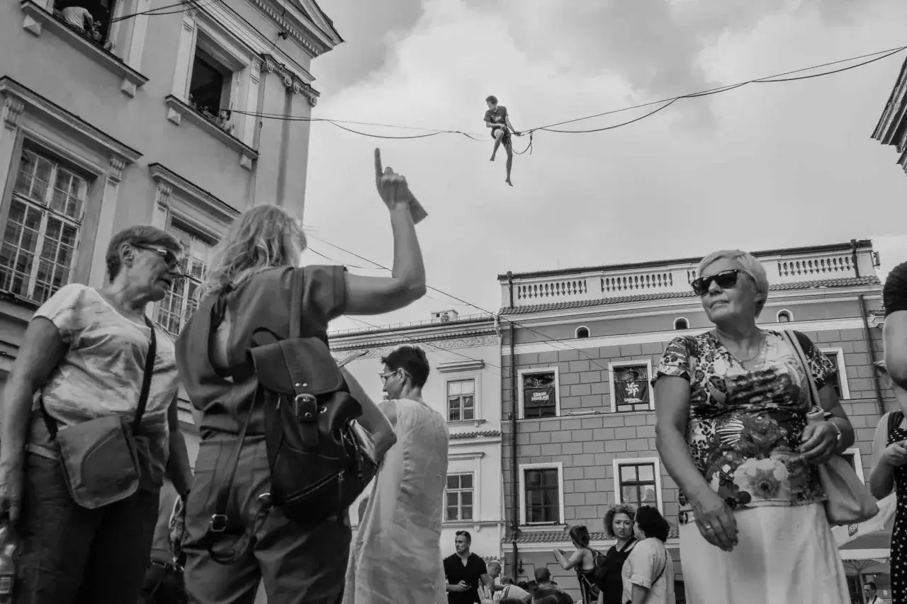 Street photography: widzowie patrzą na akrobatę balansującego na linie nad ulicą.