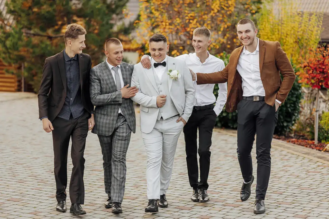 Pięciu eleganckich mężczyzn w garniturach idzie razem. Świetny pomysł na to, co zabrać na wesele, gdy chcesz wyglądać stylowo.