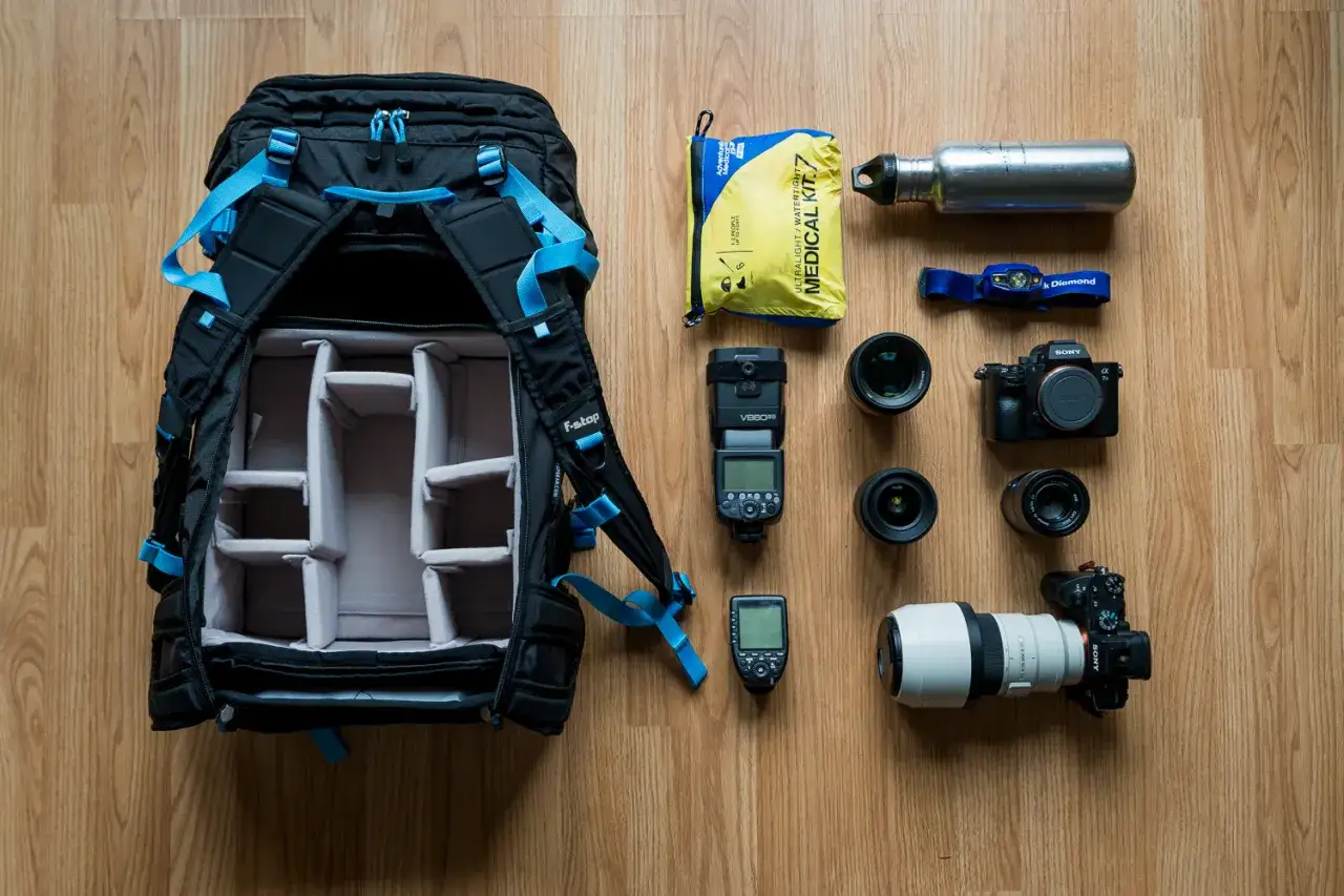 Plecak fotograficzny z akcesoriami: aparat Sony A1 II, obiektywy, lampa błyskowa, apteczka, butelka wody i latarka czołowa.